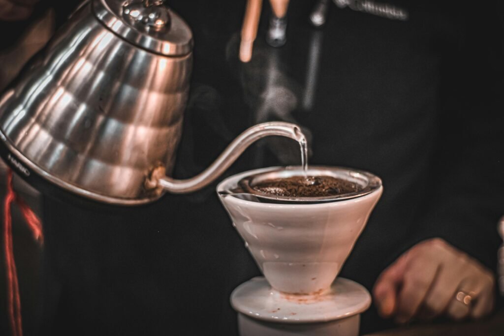 pexels-photo-14679166-14679166 Steam rises as hot water is poured over coffee grounds in a pour-over coffee maker.