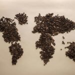 Creative world map design using coffee beans arranged on a beige background, top view