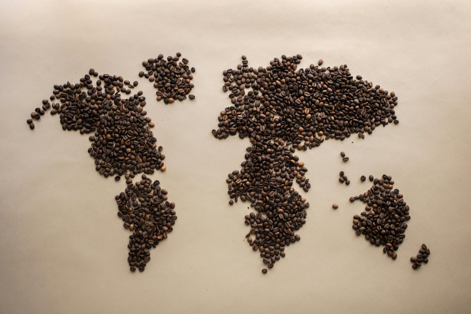 Creative world map design using coffee beans arranged on a beige background, top view